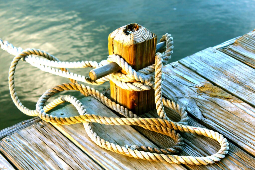 Detailed view of a coiled rope tied to a wooden dock post by the ocean.